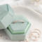  A rose gold diamond-textured stacking ring displayed inside a green velvet hexagonal ring box, with additional rings scattered beside it.